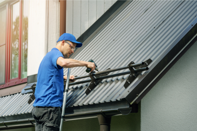 Roofer installing snow guard on metal roof